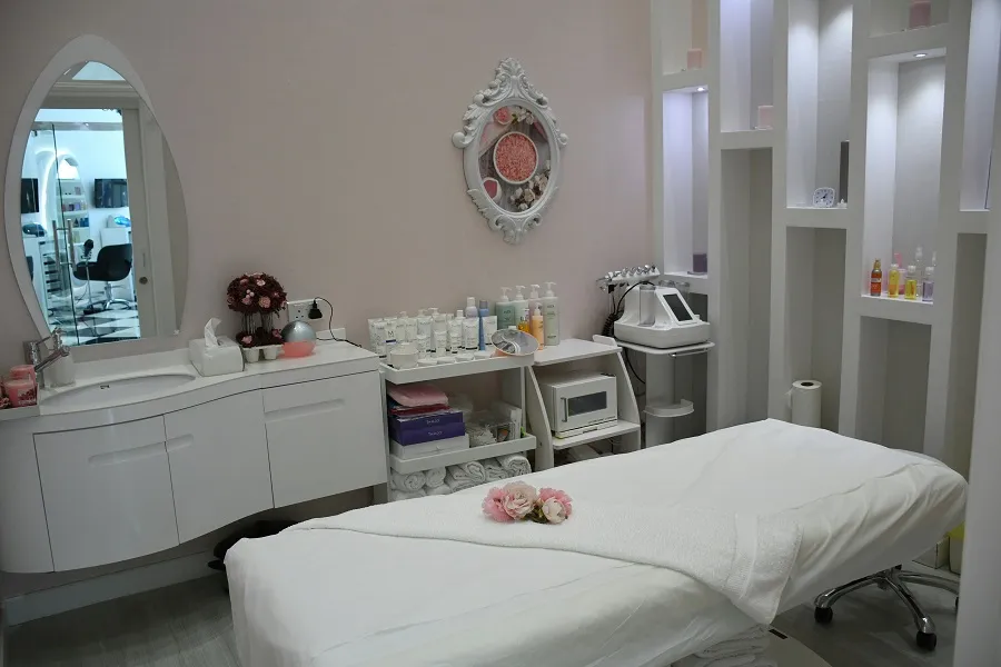A serene beauty treatment room featuring a massage table, skincare products, and elegant decor against soft pink walls